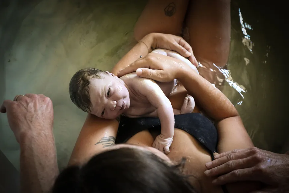 A newborn resting on mom's chest, seen from above in the birth pool