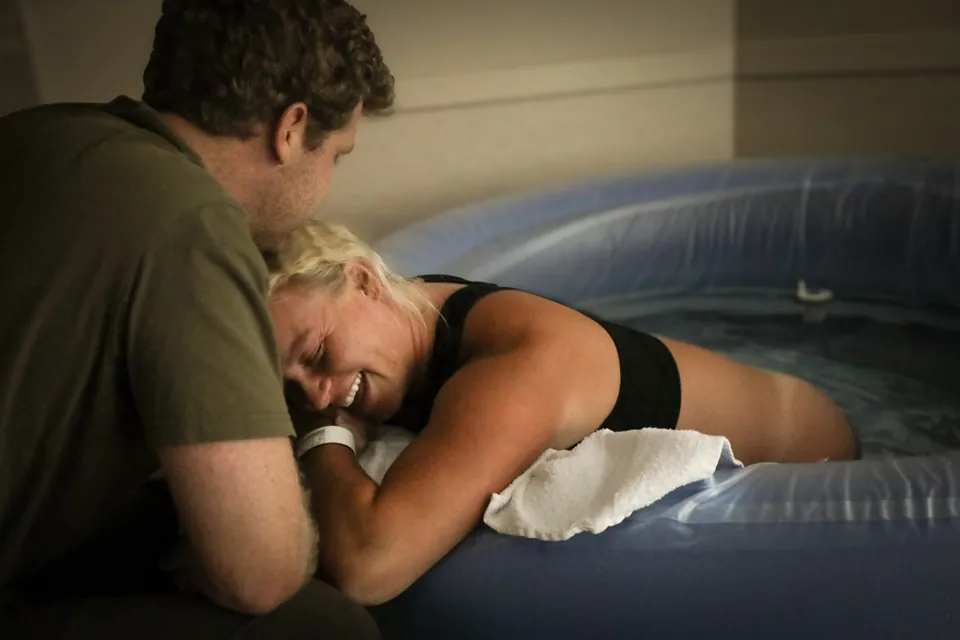 A laboring mother leans on her partner beside the birth pool