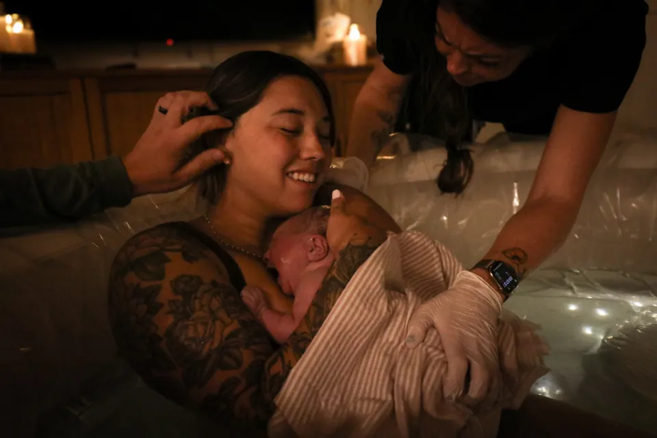 A mother cheek to cheek with her newborn by candlelight