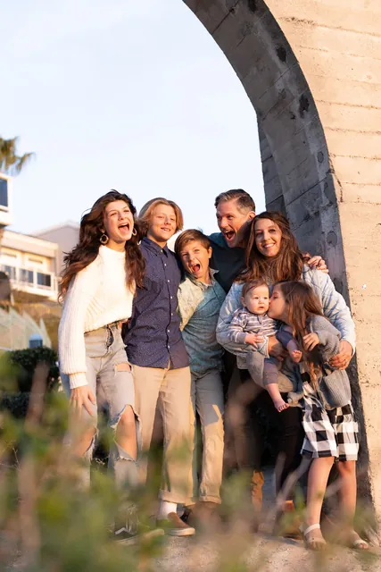 Jenn Miller, her husband and their five children laughing beside a stone arch